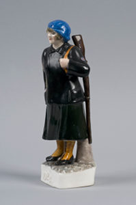 Porcelain doll of a woman with a blue hat and a rifle over her shoulder