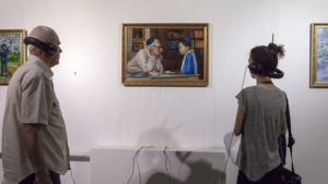 photograph of two people wearing headphones looking at a painting.
