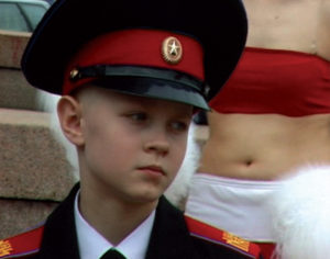 Small boy in military dress in front of woman in red bandeau