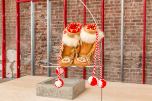 Sculpture of two moccasins on a pedestal in front of a brick wall. 