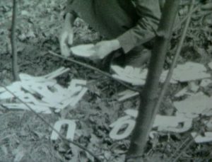 black and white image of a crouched person arranging letters on the ground. Head is out of frame.