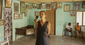 The filmmaker stands in her family’s living room in Togo, where there are portraits of other family members covering the walls.
