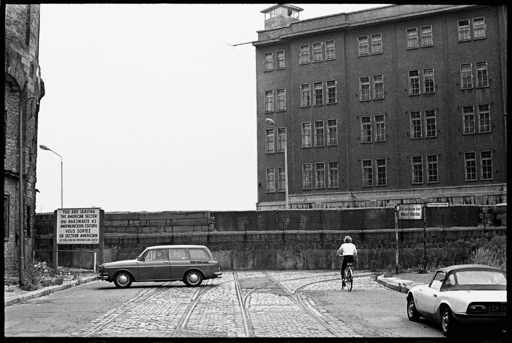 a photograph of the Berlin Wall, with a car in front and a person on a bicycle