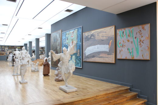 a view of the gallery with plaster sculptures in the foreground and a gray wall behind with paintings