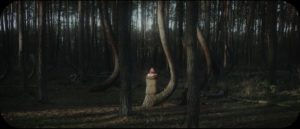 an image of a woman sitting in a darkened forest with hazy sunlight illuminating her back and the tree trunks in the foreground