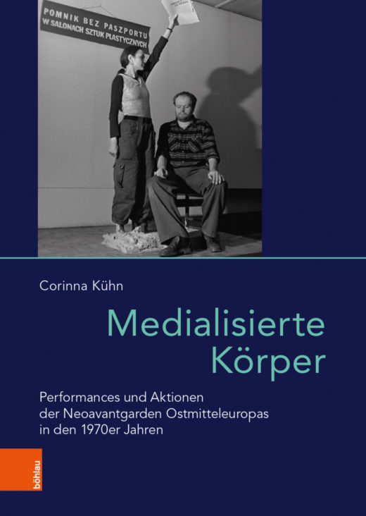 Dark blue book cover with a black and white photograph of artist duo KwieKulik, a standing woman holding papers over the head of a seated man