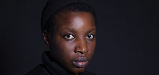 A photograph of the author, a Black woman wearing a black cap, against a dark background