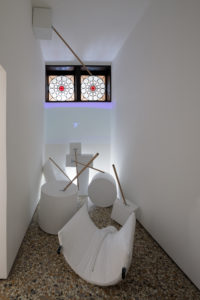 A narrow space, all white, with a number of white geometric objects in the space, with handles sticking out of them.