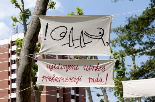 Two textile banners with signs and text are shown stretched between trees in a park