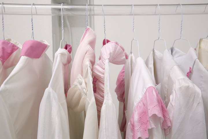 A collection of white and pink garments hanging with clothes hangers on a clear plastic tube, photographed from close up at shoulder level