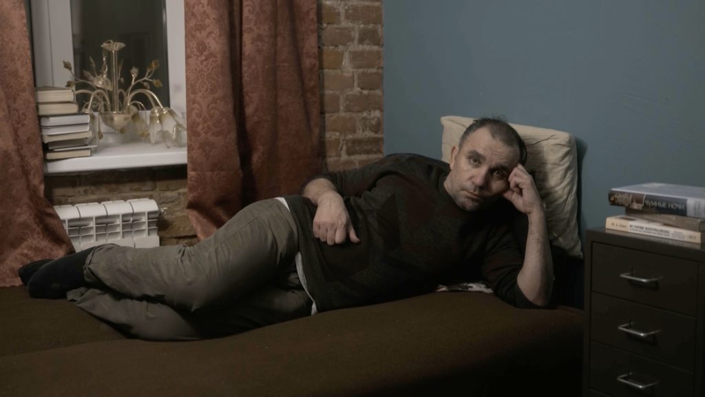 A man lying on a couch, facing the viewer.