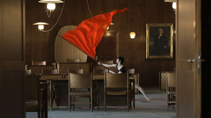 A woman waving a red flag in a richly-furnished room