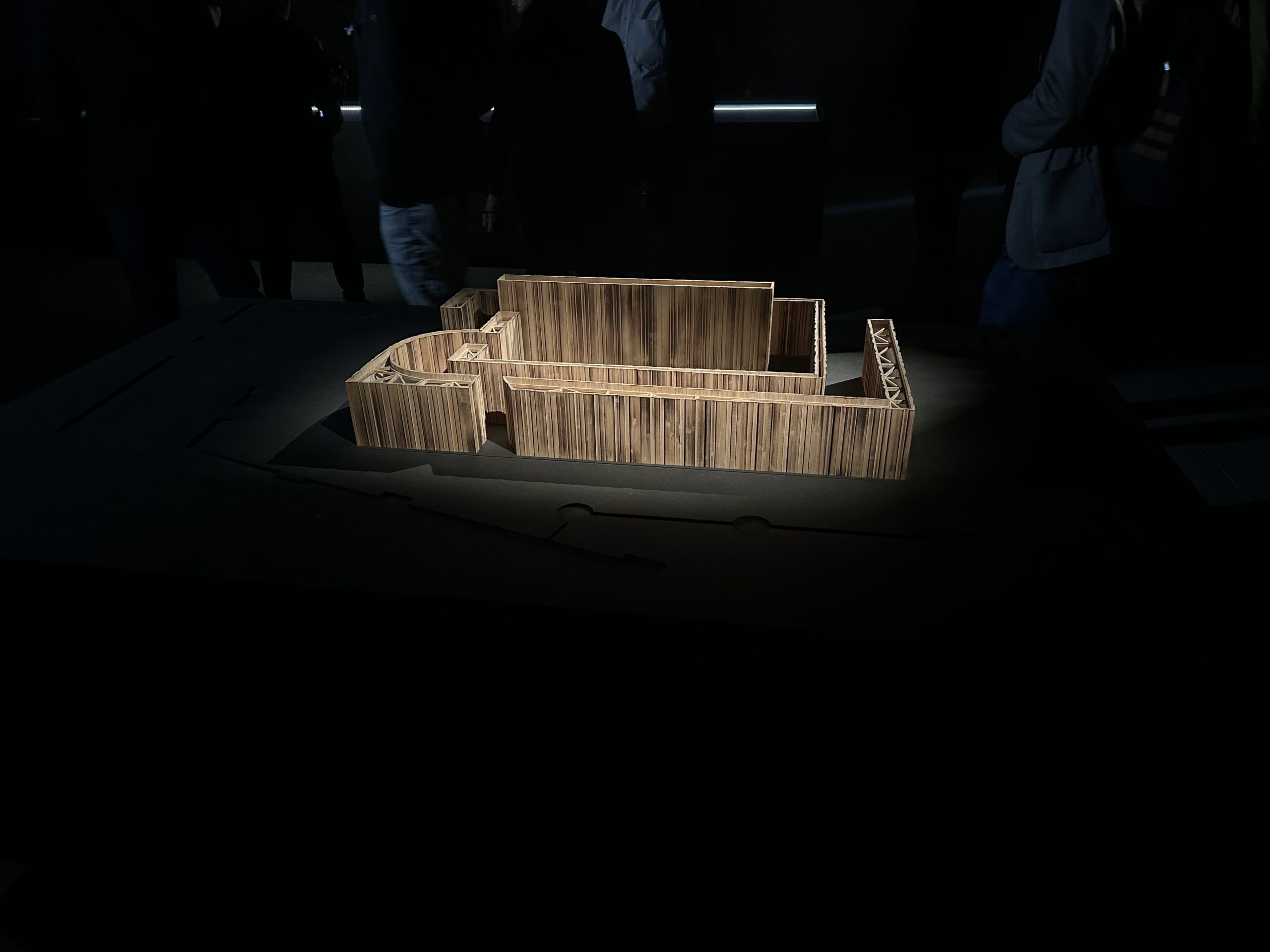 A model of a wooden labyrinth, in a darkened room, with just the labyrinth light brightly. The wood used to create the labyrinth has been darkened by burning.