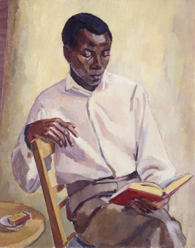A man, described as a student from Nigeria, sitting on a chair and reading a book.