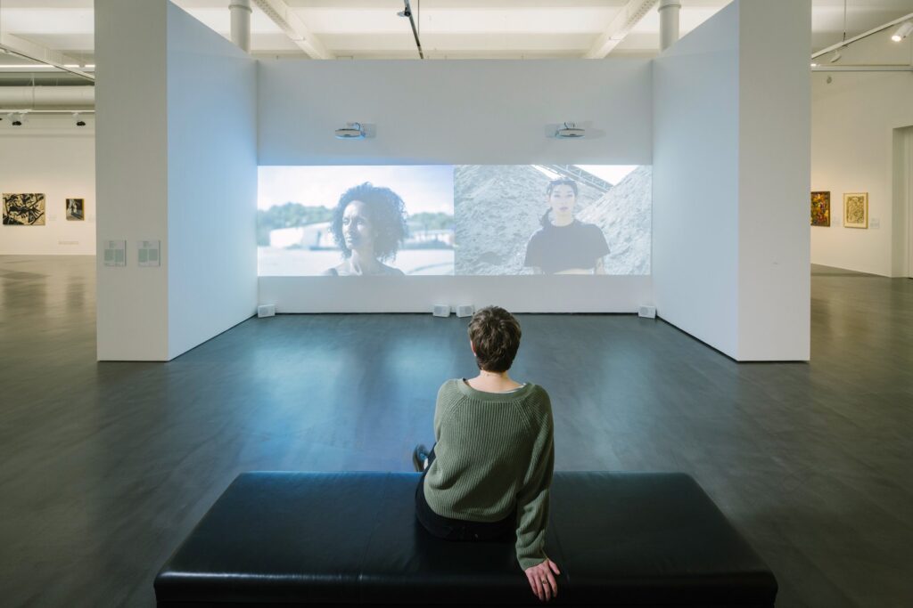 Interior of the exhibition space. A visitor watching a video installation.