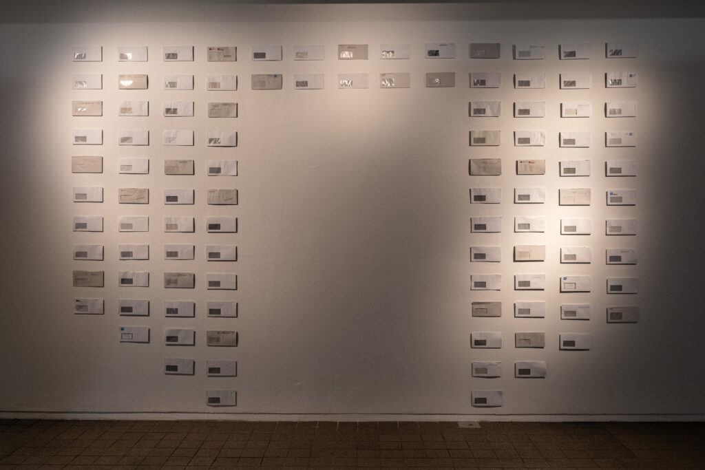 Dozens of white envelopes representing the artist’s labor in establishing herself in her new hometown, hung on the wall in an altarpiece-like arrangement.